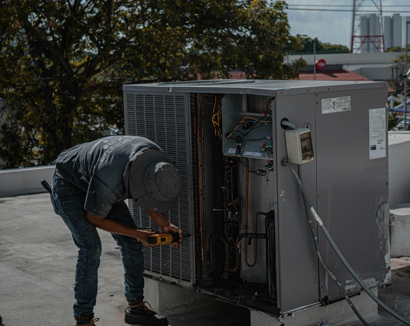 An HVAC technician working on an open rooftop condenser unit